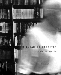 A imagem em preto e branco mostra o vulto de um homem branco de blusa e cabelo brancos passando, em direção ao lado esquerdo do local. Atrás dele, uma grande estante com livros. Na parte inferior direita da foto, a frase: “O lugar do escritor, Eder Chiodetto”. É possível que seja uma capa de um livro.