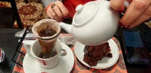 Bule de água quente preparando um café no coador de pano junto a um pedaço de bolo de chocolate