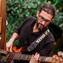 Montagem de três fotos com um musicista cada. Da esquerda para a direita: homem branco de cabelos curtos e escuros (usa blusa preta com mangas curtas e calça clara) toca guitarra em estúdio e sorri para alguém que não aparece na foto; homem branco, barbudo, de cabelos curtos e escuros (veste blusa preta de mangas longas e usa óculos) toca guitarra com o corpo inclinado para frente. Ao fundo, um espaço com plantas; homem negro (usa chapéu, óculos de grau e blusa de manga custa preta) toca bateria.