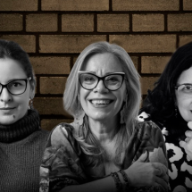 Imagem em preto e branco de três mulheres diante de uma parede de tijolos. Elas estão sorrindo e usam óculos. São, em ordem não especificada: Eliz Brito (atriz e escritora), Georgia Annes (escritora) e Marcelle Azeredo (escritora e jornalista). À esquerda, uma mulher usa suéter de gola alta e segura os óculos com uma das mãos. Ao centro, uma mulher de cabelos claros veste uma blusa estampada e sorri amplamente. À direita, outra mulher com cabelo escuro repousa o queixo sobre a mão em um gesto pensativo.