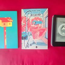 Imagem mostra três livros dispostos lado a lado sobre uma superfície vermelha. À esquerda está "Nove Casas", de Beatriz Pizani, com capa azul e a imagem de uma casa amarela sobre uma haste vermelha. No centro, o livro "Dançando na Varanda", de Nicole Ayres, com ilustração colorida de uma mulher dançando em uma varanda. À direita, um e-reader exibe a capa do livro "A Cápsula", de Carolina Fraiz, com ilustração em preto e branco de uma figura feminina em posição fetal dentro de uma cápsula.