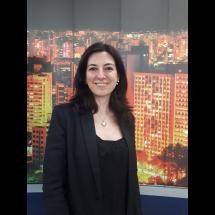A jornalista, palestrante, escritora e consultora de comunicação Vanessa Guimarães sorri levemente diante de um painel com imagem de prédios iluminados à noite, compondo uma paisagem urbana. Ela tem cabelos escuros e lisos, na altura dos ombros, e veste blazer escuro sobre blusa preta rendada. Usa colar com pingente em formato de coração. A imagem transmite profissionalismo, simpatia e confiança.