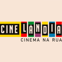 A imagem exibe a identidade visual do projeto Cinelândia – Cinema na Rua. O nome “Cinelândia” aparece em letras maiúsculas dentro de retângulos coloridos (amarelo, vermelho, verde, roxo, amarelo, azul e vermelho), com fundo preto para as letras. Abaixo, em letras pretas, está o subtítulo “Cinema na Rua”, sobre um fundo bege claro.