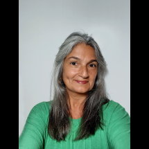 Retrato da arteterapeuta de base junguiana Ana Cristina Marques Sabioni. Mulher de meia-idade, pele clara e cabelos longos grisalhos, repartidos ao meio e soltos sobre os ombros. Olhos castanhos, leve sorriso e expressão acolhedora. Usa blusa verde e pequeno brinco dourado. A fotografia é em plano próximo, com fundo neutro claro e iluminação suave, transmitindo serenidade e proximidade.
