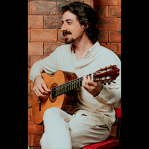 Marcello Cascino (voz e violão) aparece sentado tocando violão. Vestido com roupas claras, o músico é fotografado de perfil diante de uma parede de tijolos aparentes.  