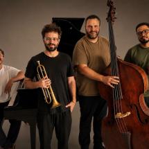 Os músicos Ciro Magnani, Joe Ze Pepe, Domenico Botelho e Michel Nascimento posam juntos. Ciro está ao lado de um piano; Joe segura um trompete; Domenico aparece junto ao contrabaixo; e Michel segura uma baqueta. Os quatro são fotografados diante de um fundo neutro.