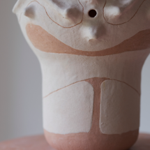 Arte de divulgação da exposição Zumbido (arte sonora). Ao fundo, detalhe de um objeto escultórico em tons claros e rosados, com formas orgânicas, linhas sinuosas e um pequeno orifício circular, cuja aparência lembra uma colmeia.