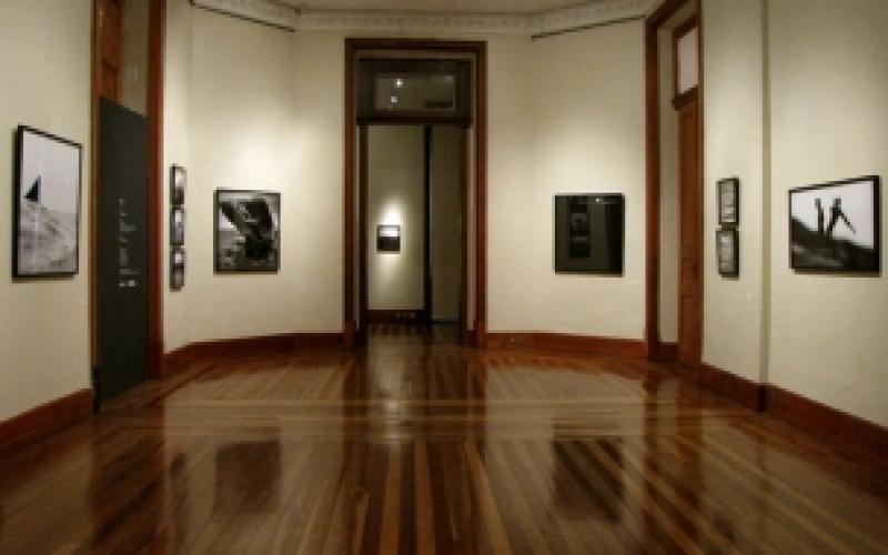 A foto mostra um recorte de uma sala da época colonial, com cadeiras para o público e um parlamento, tudo em madeira. Há lustres dourados; as paredes e teto são desenhadas e com arabescos clássicos. O local é a Sala de Sessões do Centro Cultural Justiça Federal.