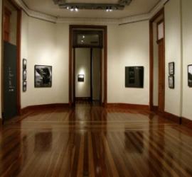 A foto mostra um recorte de uma sala da época colonial, com cadeiras para o público e um parlamento, tudo em madeira. Há lustres dourados; as paredes e teto são desenhadas e com arabescos clássicos. O local é a Sala de Sessões do Centro Cultural Justiça Federal.