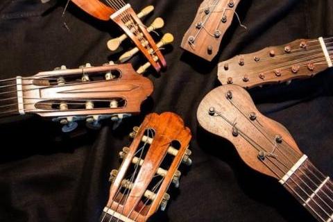 Sobre um fundo de tecido marrom, dispostos em círculo, cinco instrumentos de corda (violão, viola…) dos quais só aparece a parte superior: mão, tarraxas, pestana e parte dos braços com as cordas.