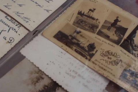 Fotografia em close de documentos e imagens antigas sobre uma superfície. Em destaque, um cartão postal envelhecido com pequenas fotografias e a inscrição “Recuerdo de Mendoza”. Ao redor, há papéis com bordas desgastadas e trechos de escrita à mão, sugerindo correspondências antigas. A composição e os tons amarelados transmitem sensação de memória, arquivo e passagem do tempo.