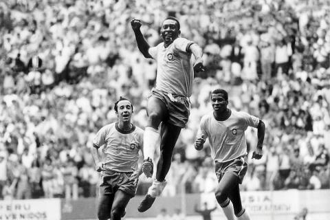 Fotografia histórica em preto e branco conhecida como “Três no Tri”, de Orlando Abrunhosa. Pelé aparece ao centro, saltando com o punho erguido em comemoração, enquanto Tostão e Jairzinho correm logo atrás. Ao fundo, a arquibancada lotada reforça o clima de celebração da conquista da Copa do Mundo de 1970.
