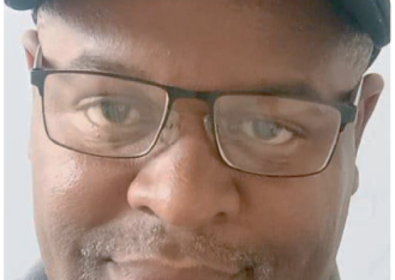 Imagem com fundo branco. À esquerda, foto de um homem de óculos, boné preto e expressão sorridente.