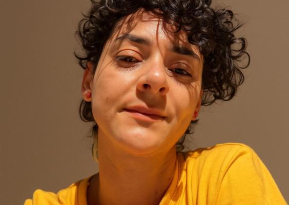 Retrato da estagiária Rochelle Silveira. Com cabelos curtos e cacheados, ela veste camiseta amarela e olha para a câmera com expressão serena.