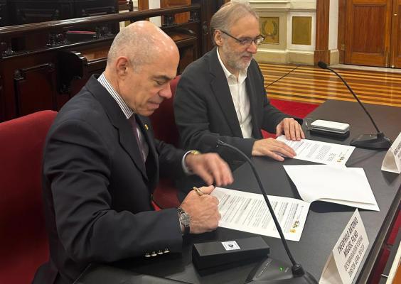 Na Sala de Sessões do CCJF, o diretor-geral do Centro Cultural Justiça Federal, Dr. Theophilo Miguel Filho, assina o protocolo de intenções que formaliza a parceria com a Fundação Biblioteca Nacional. Ao seu lado, Marco Aurélio Lucchesi, presidente da Biblioteca Nacional, acompanha a assinatura com os documentos à sua frente. Sobre a mesa há microfones, pastas e folhas utilizadas na cerimônia.