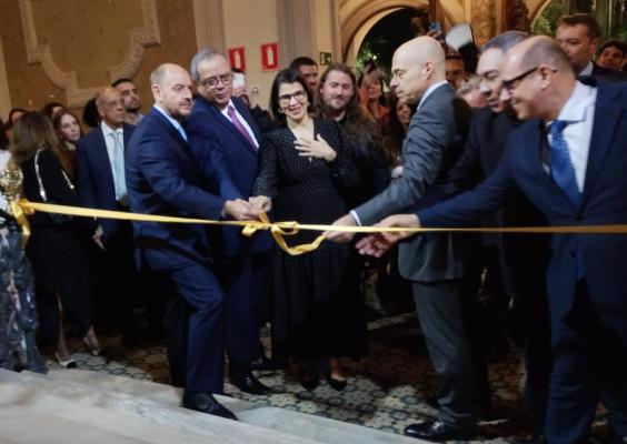 No pé da escadaria principal do CCJF, autoridades e curadores participam da abertura da exposição Coleção Ingá: Brasil plural. Reunidos diante de um grupo de pessoas, alguns deles seguram uma fita amarela estendida à frente e realizam o corte simbólico que marca a inauguração da mostra. Ao fundo, o ambiente histórico do CCJF e o público acompanham a cerimônia.