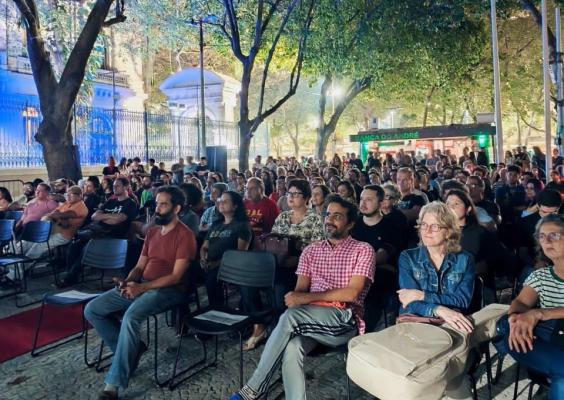 Grande público ocupa as cadeiras do Cinelândia Cinema na Rua, em sessão ao ar livre do documentário Apocalipse segundo Baby. Sob as árvores e a iluminação noturna, dezenas de pessoas acompanham a programação, distribuídas em várias fileiras que se estendem pela área externa do CCJF. Após a exibição, o público participou de um bate-papo com a cantora Baby e o diretor do documentário.