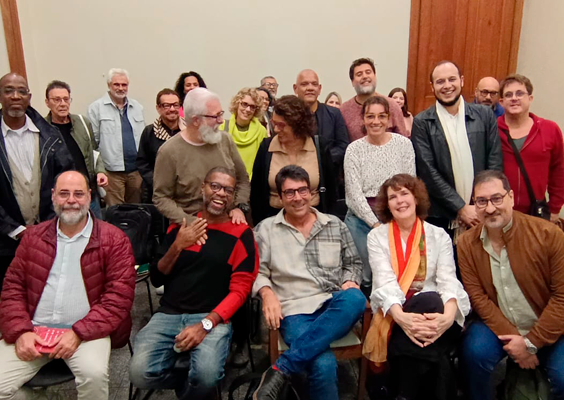 Registro da edição de julho do projeto Ocupação Poética. O poeta homenageado Alberto Pucheu aparece sentado ao centro, cercado pelos convidados Cláudio Oliveira, Caio Meira e Cris Mayrink, pelo mediador Paulo Sabino e por participantes do encontro. O grupo, formado por cerca de vinte pessoas, posa reunido para a fotografia, com parte dos participantes sentada à frente e os demais em pé ao fundo.