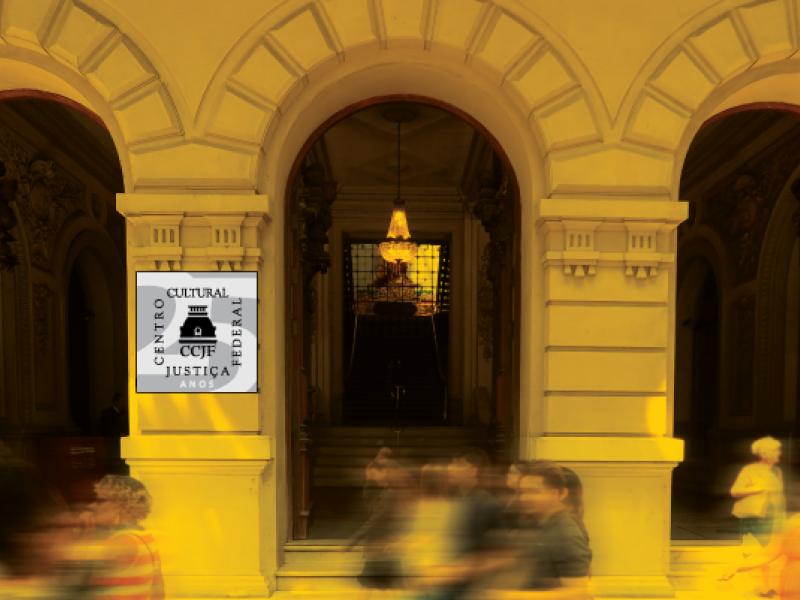 A imagem mostra a fachada de um edifício histórico com arcos altos, colunas e detalhes clássicos. No centro, uma escadaria leva a uma grande porta de madeira, com um lustre suspenso acima. Uma placa à esquerda diz: "CCJF. Centro Cultural Justiça Federal.