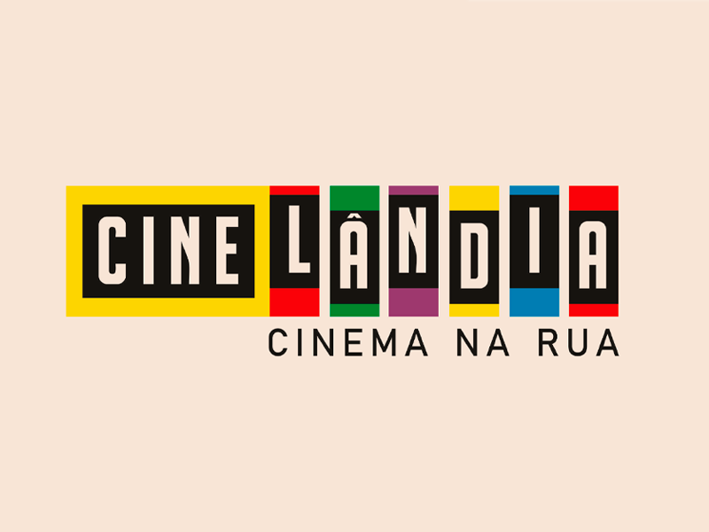 A imagem exibe a identidade visual do projeto Cinelândia – Cinema na Rua. O nome “Cinelândia” aparece em letras maiúsculas dentro de retângulos coloridos (amarelo, vermelho, verde, roxo, amarelo, azul e vermelho), com fundo preto para as letras. Abaixo, em letras pretas, está o subtítulo “Cinema na Rua”, sobre um fundo bege claro.