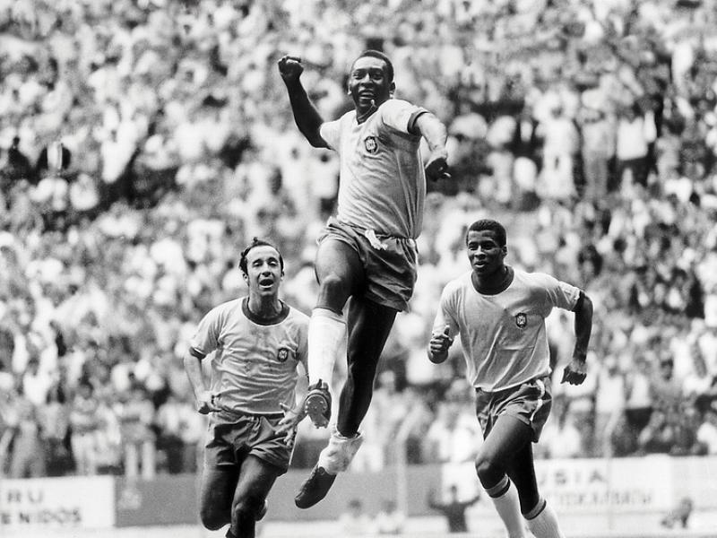 Fotografia histórica em preto e branco conhecida como “Três no Tri”, de Orlando Abrunhosa. Pelé aparece ao centro, saltando com o punho erguido em comemoração, enquanto Tostão e Jairzinho correm logo atrás. Ao fundo, a arquibancada lotada reforça o clima de celebração da conquista da Copa do Mundo de 1970.