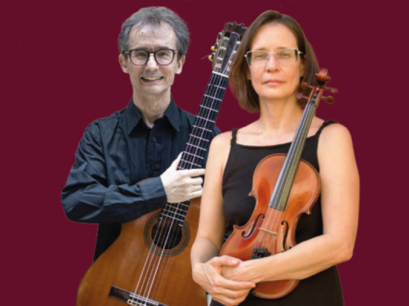 A violinista Mariana Salles e o violonista Clayton Vetromilla posam diante de um fundo bordô. À frente, Mariana segura um violino com as duas mãos e veste blusa preta sem mangas. Ao fundo, Clayton sorri para a câmera enquanto apoia um violão clássico na altura do peito. Ambos usam óculos e roupas escuras, e os instrumentos de madeira se destacam na composição.