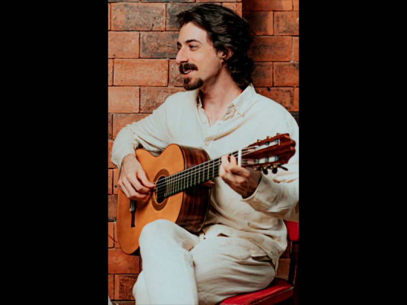 Marcello Cascino (voz e violão) aparece sentado tocando violão. Vestido com roupas claras, o músico é fotografado de perfil diante de uma parede de tijolos aparentes.  