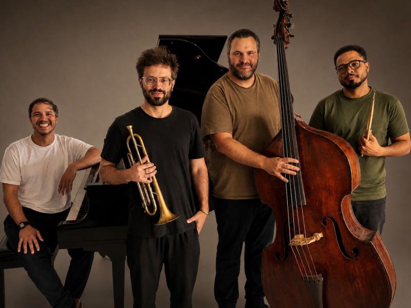 Os músicos Ciro Magnani, Joe Ze Pepe, Domenico Botelho e Michel Nascimento posam juntos. Ciro está ao lado de um piano; Joe segura um trompete; Domenico aparece junto ao contrabaixo; e Michel segura uma baqueta. Os quatro são fotografados diante de um fundo neutro.